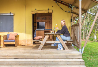 Kvinde nyder en drink ved et picnicbord foran safari-teltet 'De Bos Tent' på Gooise Heide, Holland.