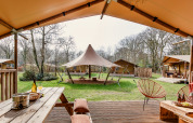 Blick von einer Safarizelt-Terrasse mit Holzmöbeln und Zelten auf einem grünem Campingplatz im Wald.