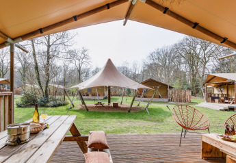 Vue d'une terrasse de tente safari avec mobilier en bois et grandes tentes sur un camping vert boisé.