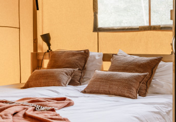 Lit douillet avec coussins bruns et couverture dans une tente safari chaleureusement éclairée par la lumière.
