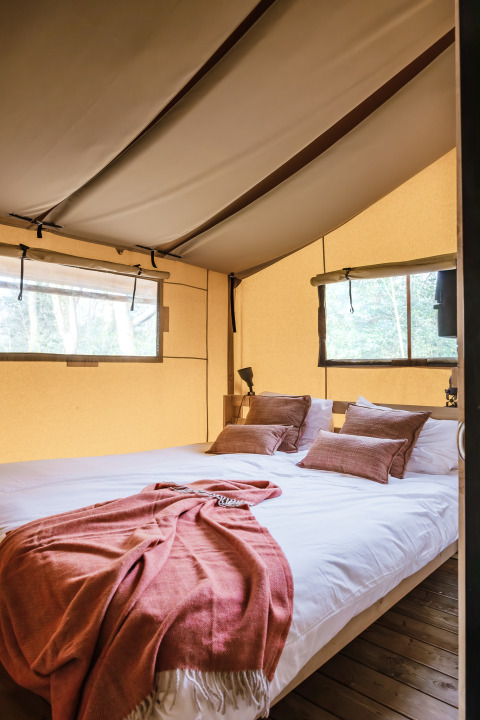 Interno di tenda safari moderna con letto matrimoniale, pavimento in legno e finestre che danno sul verde.