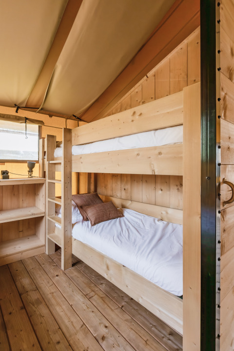 Intérieur d'une tente safari avec lits superposés en bois clair, étagère et plancher en bois.