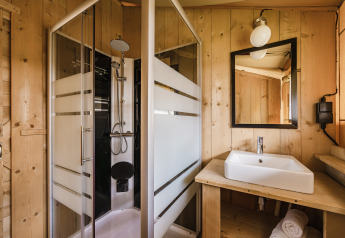 Salle de bain dans une tente safari avec cabine de douche, lavabo, miroir et murs en bois naturel.