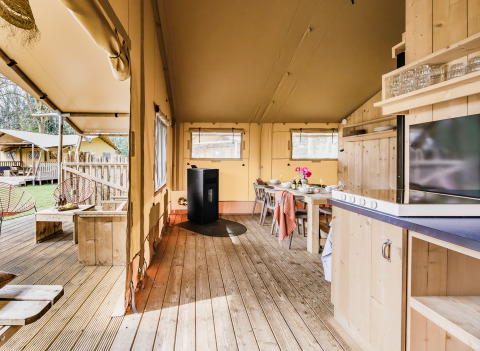 Vue intérieure d'une tente safari confortable avec plancher en bois, cuisine, coin repas et terrasse extérieure.