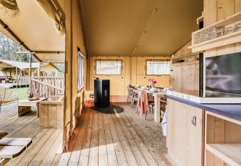 Vue intérieure d'une tente safari confortable avec plancher en bois, cuisine, coin repas et terrasse extérieure.