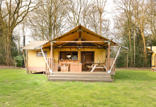 Tenda safari con veranda in legno e area pranzo esterna, immersa nel verde e circondata da alberi.