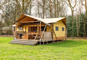 Safari-Zelt mit Holzterrasse und Außensitzplätzen, gelegen in einer grünen, bewaldeten Lichtung.