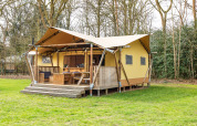 Safari-Zelt mit Holzterrasse und Außensitzplätzen, gelegen in einer grünen, bewaldeten Lichtung.