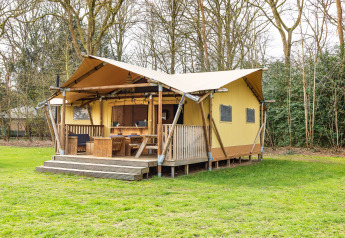 Tente safari avec terrasse en bois et coin salon extérieur, située dans une clairière entourée d’arbres.