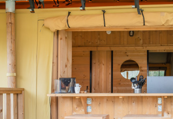 Interieur van een safaritent met houten meubels, bar, wijnflessen en fruit op de tafel op de voorgrond.
