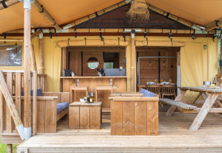 Area salotto esterna di una tenda safari con arredi in legno, tavolo e atmosfera rustica e accogliente.
