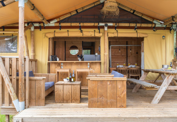 Buitenruimte van een safaritent met houten meubels, tafel en een warme, rustieke uitstraling.