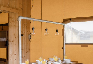 Interno di una tenda safari con tavolo in legno apparecchiato per la colazione e luci sospese.