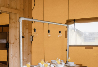 Gezellig ingerichte safaritent met houten tafel, ontbijtservies en rustieke hanglampen bovenaan.