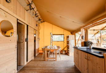 Innenansicht eines luxuriösen Safari-Zelts mit Holzmöbeln, Esstisch und offener Küchenzeile.