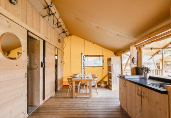 Binnenzicht van een luxueuze safaritent met houten interieur, eettafel en open keukenruimte.