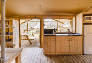 Area cucina in una tenda safari con arredi in legno, vista su tavolo da picnic e altre tende all’esterno.
