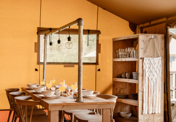 Safari-Zelt-Essbereich mit Holztisch, Stühlen, Geschirrregal und stimmungsvoller Beleuchtung.