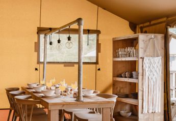 Eetruimte in safaritent met houten tafel, stoelen, servieskast en warme, sfeervolle verlichting.