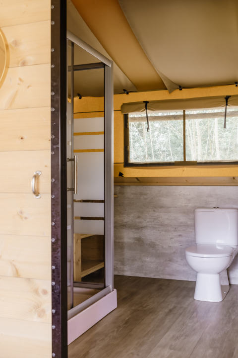 Badeværelse i et safaritelte med moderne bruser, toilet og stort vindue med udsigt til naturen.