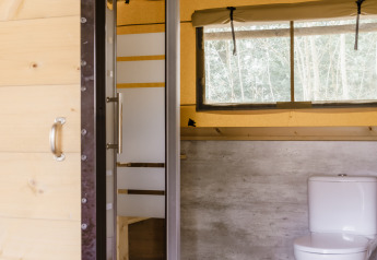 Badkamer in een safaritent met moderne douche, toilet en groot raam met zicht op de natuur.
