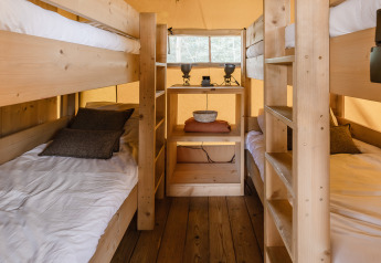 Binnenzicht van een safaritentkamer met houten vloer, stapelbedden en een klein rek aan het einde.