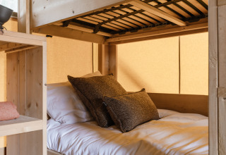 Letto accogliente con cuscini all’interno di una tenda safari, arredi in legno e luce soffusa