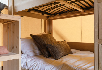 Gezellig bed met kussens in een safaritent, houten inrichting en warme natuurlijke lichtinval