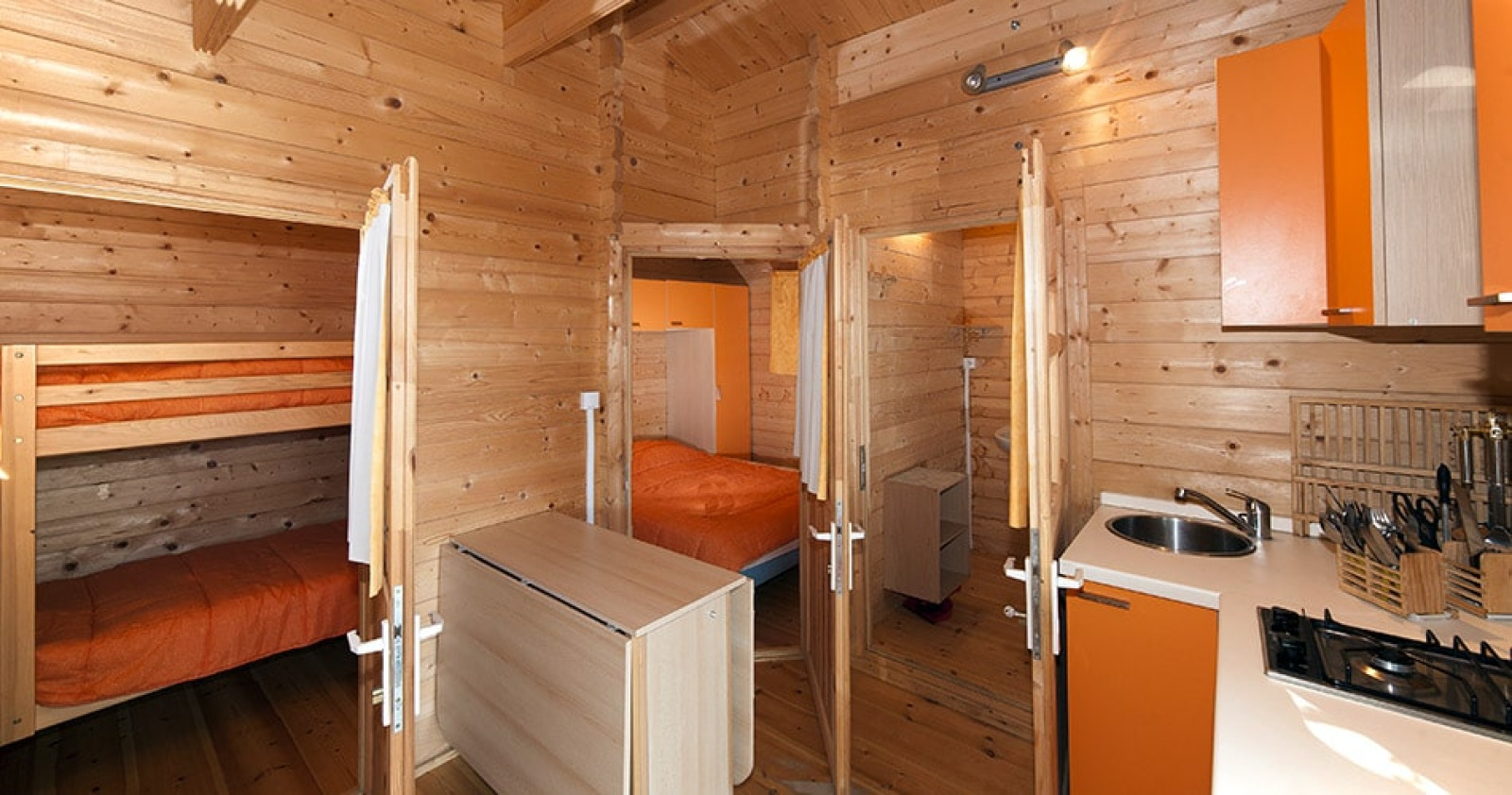 Houten Chalet Marina cabin met stapelbedden en keuken bij Camping Merendella in Frankrijk, sfeervol verlicht.