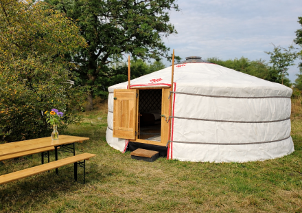 Mongoolse joert in de natuur met open houten deur, picknickbank, tafel en vaas bloemen.