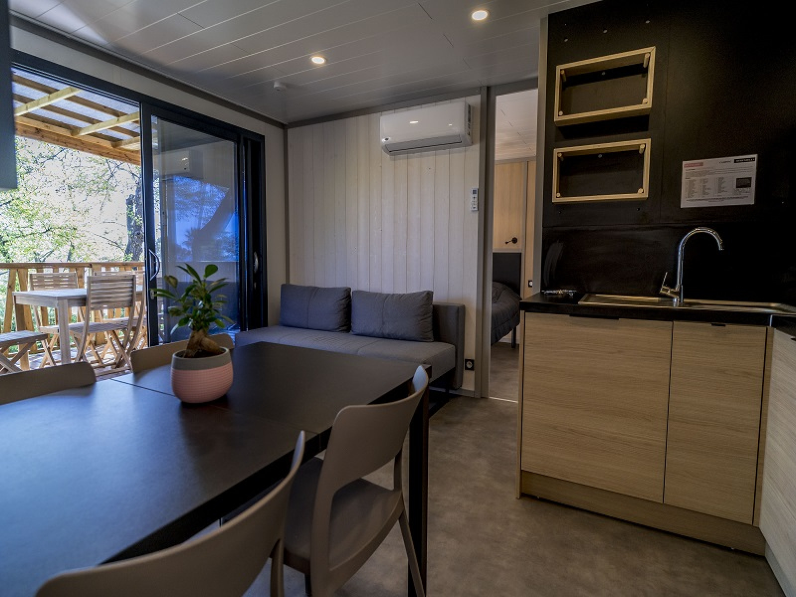 Modern lodge-interieur met eethoek, bank, kitchenette en terras met zeezicht bij Camping Merendella, Frankrijk.