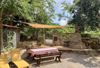 Buitenruimte met tafel, banken, ligstoelen en zonnescherm bij Agricampeggio La Prugnola in Toscane.