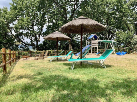 Buitenruimte met ligstoelen, rieten parasols en speeltuin bij Agricampeggio La Prugnola in Toscane, Italië.