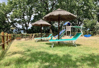 Buitenruimte met ligstoelen, rieten parasols en speeltuin bij Agricampeggio La Prugnola in Toscane, Italië.