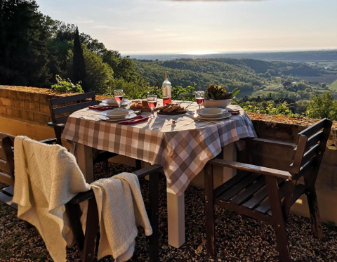 Buitentafel met ruitjeslaken en stoelen, zicht op Toscaanse heuvels bij zonsondergang, Italië.