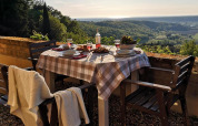 Buitentafel met ruitjeslaken en stoelen, zicht op Toscaanse heuvels bij zonsondergang, Italië.