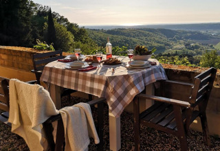 Mesa de comedor al aire libre con manta, vino rosado y vistas a colinas verdes en la Toscana, Italia.