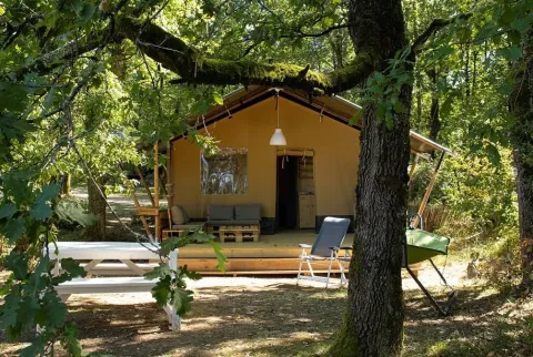 Safaritent met privébadkamer, houten terras en buitenzitje, midden in een bosrijke omgeving.