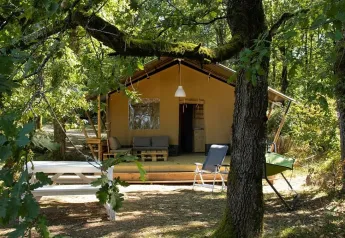 Safarizelt mit eigenem Bad, umgeben von Bäumen, mit Veranda und Gartenmöbeln im Grünen.