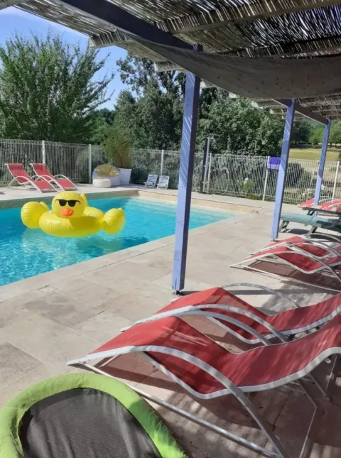 Buitenzwembad bij Domaine de La Velle, Occitanië, Frankrijk, met rode ligstoelen en gele eend drijver.
