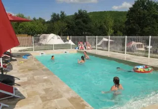 Familier nyder en solrig dag ved swimmingpoolen på Domaine de La Velle i Occitanie, Frankrig, omgivet af telte.