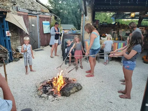 Familier og børn rister skumfiduser rundt om et lejrbål på Domaine de La Velle i Occitanie, Frankrig.