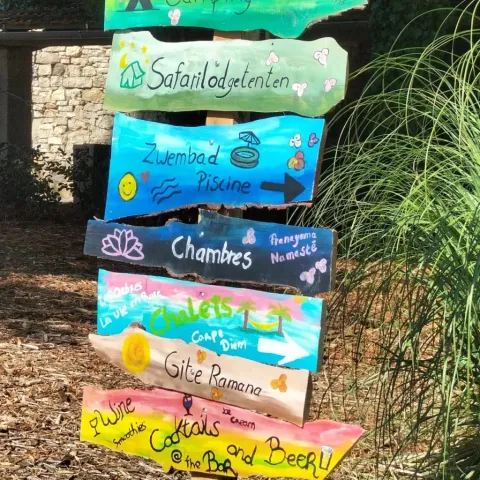 Farverig træskilt i Domaine de La Velle, Occitanie, med vejvisere til pool, bar og overnatning.