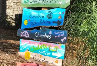 Farverig træskilt i Domaine de La Velle, Occitanie, med vejvisere til pool, bar og overnatning.