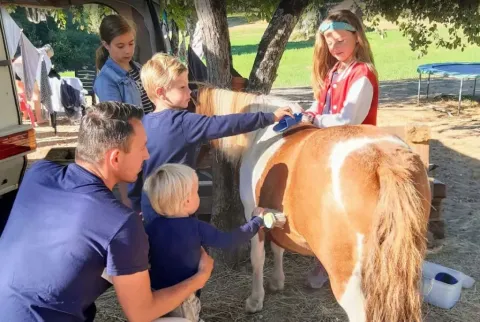 Gezin met kinderen verzorgt een pony onder bomen bij Domaine de La Velle, vakantiepark in Occitanië, Frankrijk.