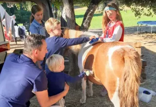 Familie med børn plejer en pony under træer i Domaine de La Velle, et feriepark i Occitanie, Frankrig.