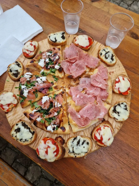 Houten plank met pizza en bruschetta, geserveerd met bekers water bij Agricampeggio Tasteria in Marche, Italië.