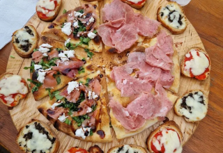 Et træfad med pizza og bruschetta, serveret med plastikglas vand på et bord på Agricampeggio Tasteria i Marche.