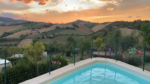 Vista al tramonto sulle colline marchigiane dalla piscina dell'Agricampeggio Tasteria, parco vacanze in Italia.