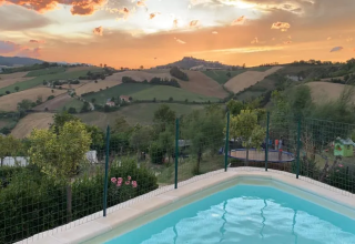 Vista al tramonto sulle colline marchigiane dalla piscina dell'Agricampeggio Tasteria, parco vacanze in Italia.